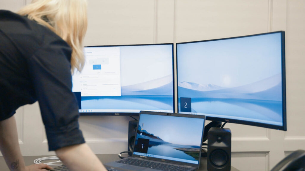 Person working on a computer with multiple monitors showing a serene landscape.